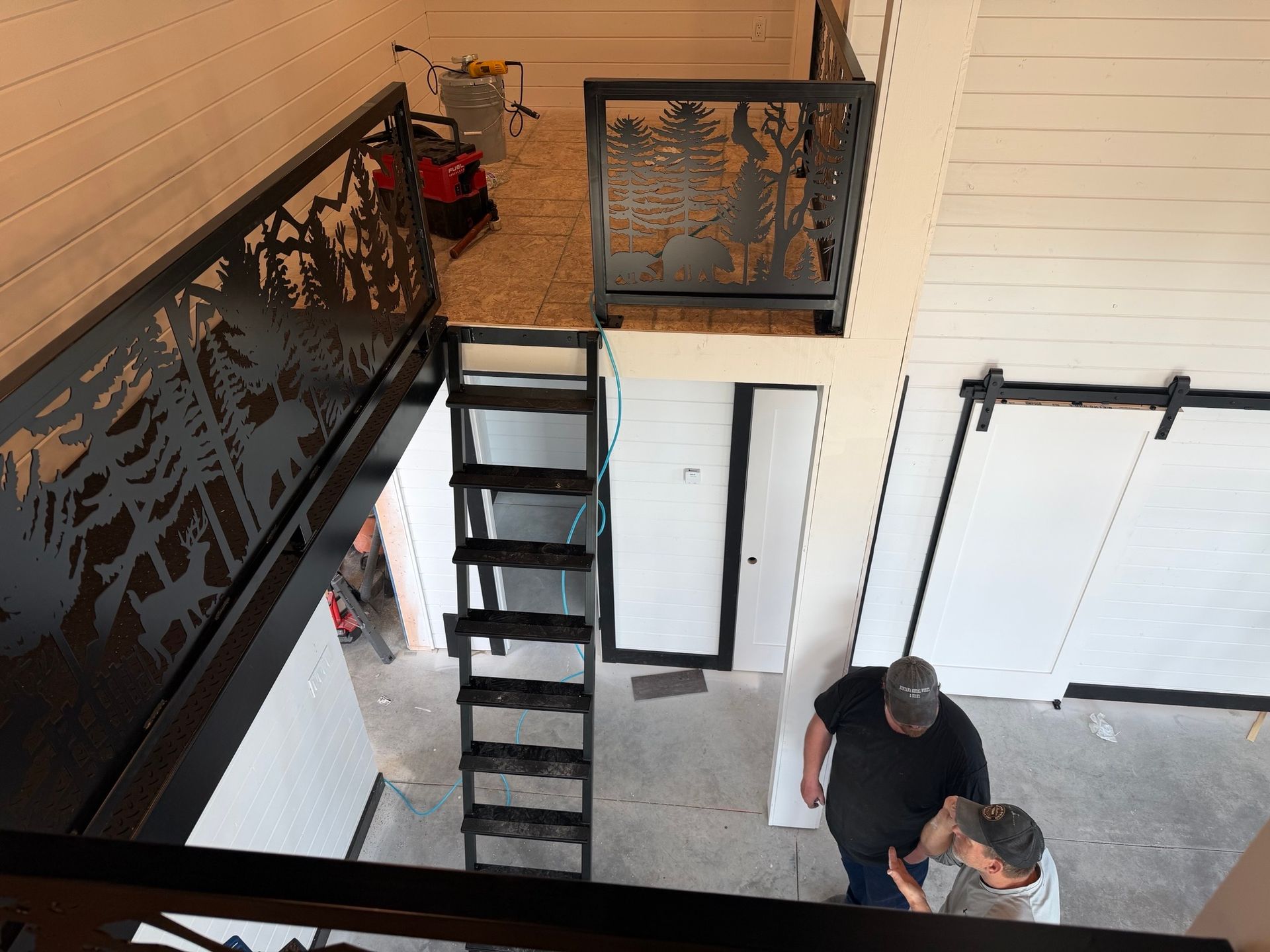 Indoor stairwell with black metal stairs and railing; two people stand at the bottom near a doorway.