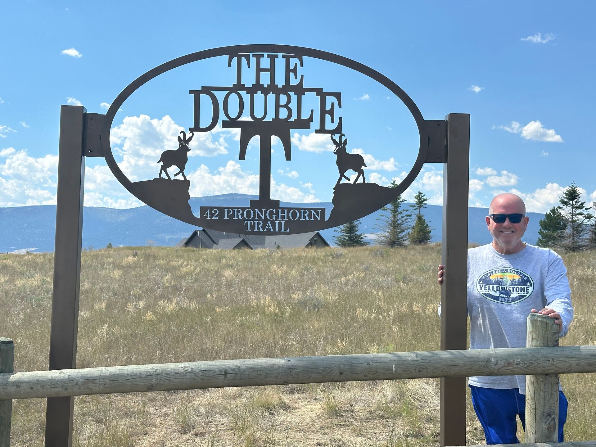 Man posing by The Double T sign in a grassy field under a blue sky