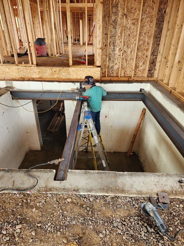 Worker on ladder inspecting beams inside an unfinished building with exposed framing.
