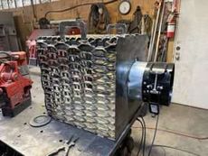 Large metal workshop machine with coiled front grille and black motor housing in a garage-like shop