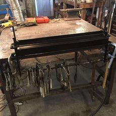 Workshop metal table with hanging clamps and tools in a cluttered garage