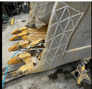 Yellow robot gripper tipped on its side, with exposed cables and patterned metal housing on a workshop floor