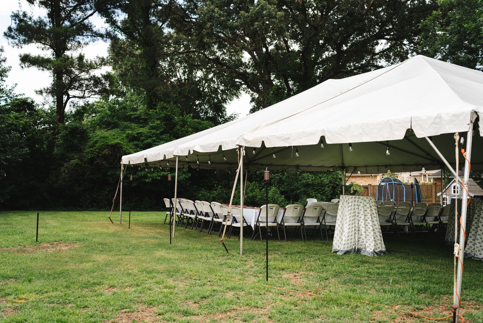 White pole tent with string lights over rows of tables and chairs on a lawn.