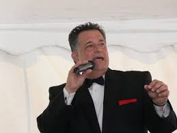 Man in black suit singing into a microphone. Red pocket square.