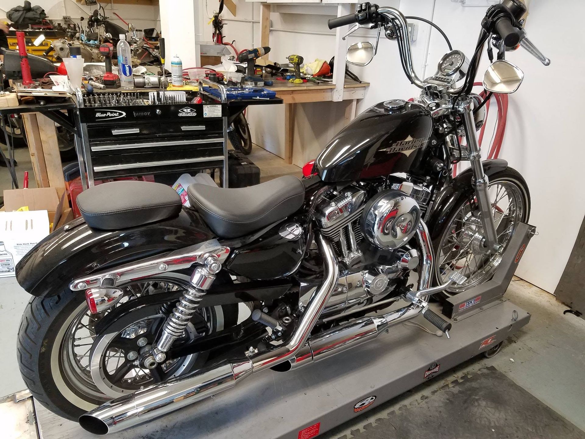 Chrome motorcycle exhaust pipes and tools on a workbench in a garage.