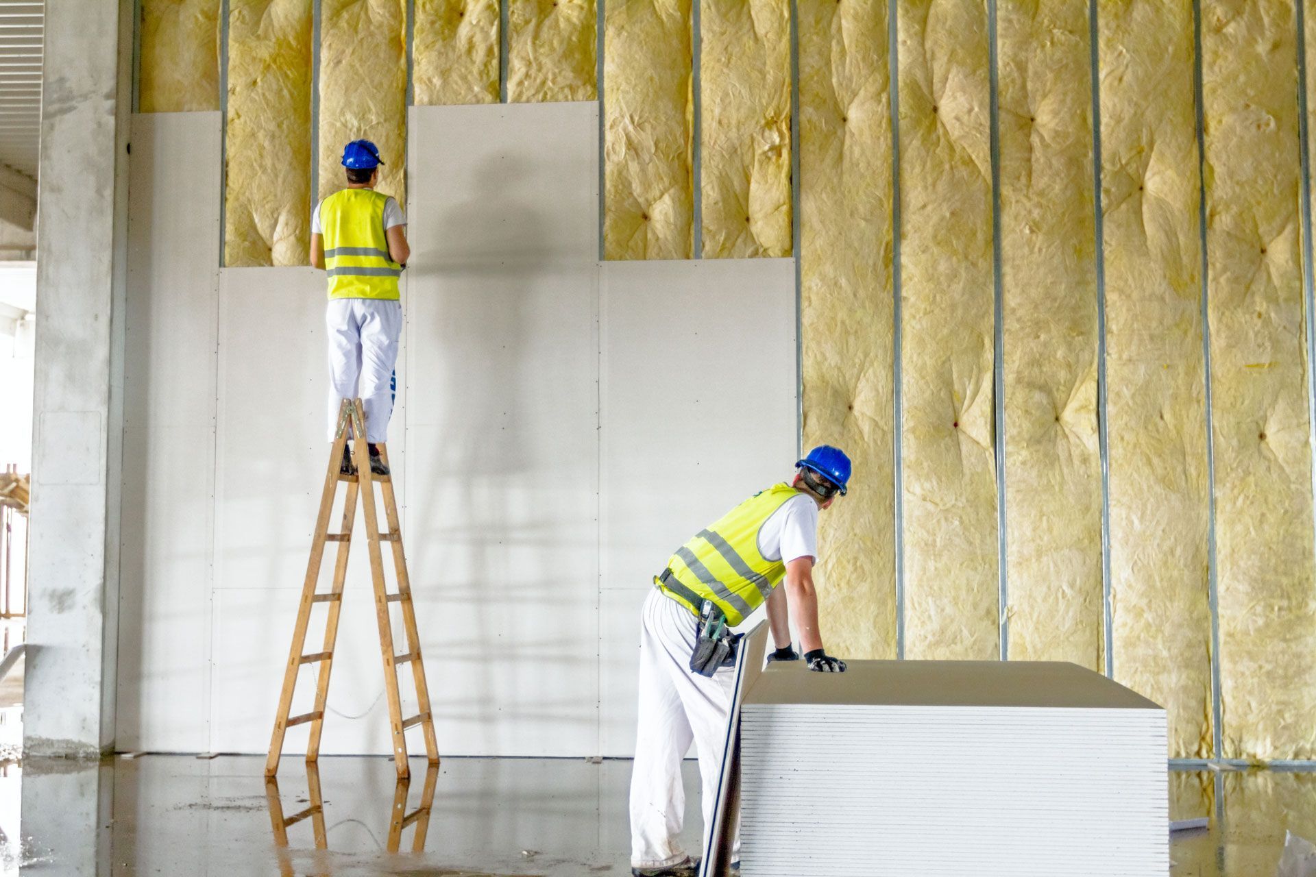 Two workers installing insulation and drywall inside a building under construction