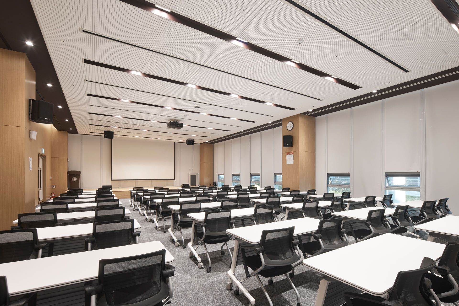 Empty modern classroom with rows of black chairs, white tables, and a patterned ceiling