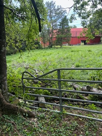 Wooded path with metal gate, stone steps, and a red barn in the background