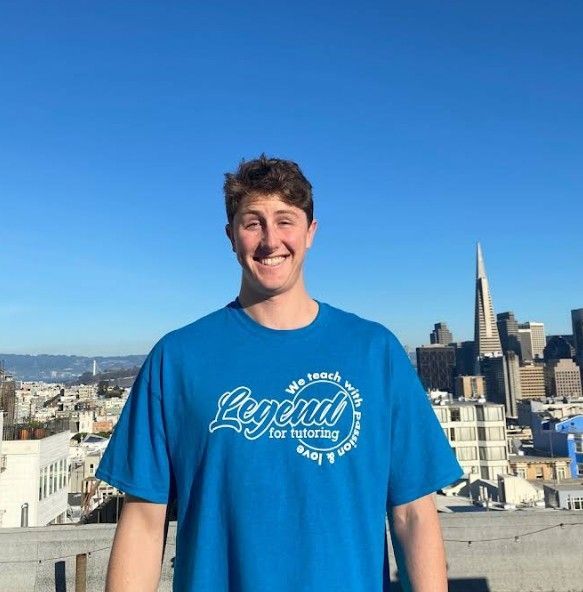 Man in blue shirt smiling on a rooftop in San Francisco, cityscape in background.