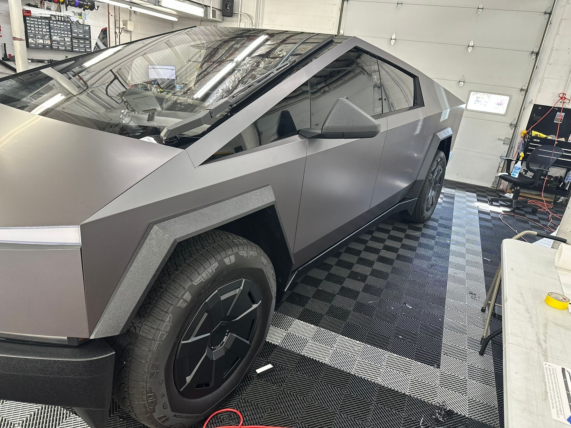 Gray Tesla Cybertruck in a garage, matte finish, angled view.