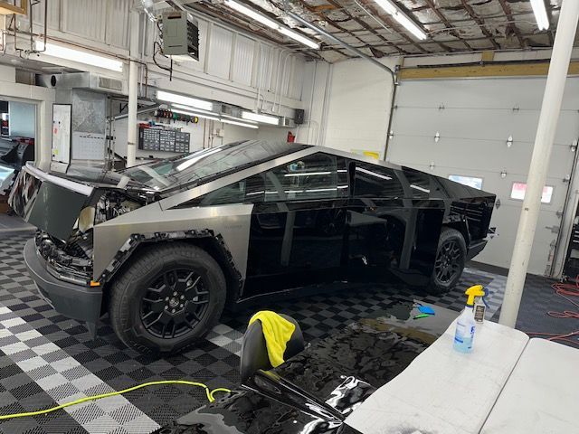 Tesla Cybertruck being worked on in a garage. Black panels and windows, silver body, open doors.