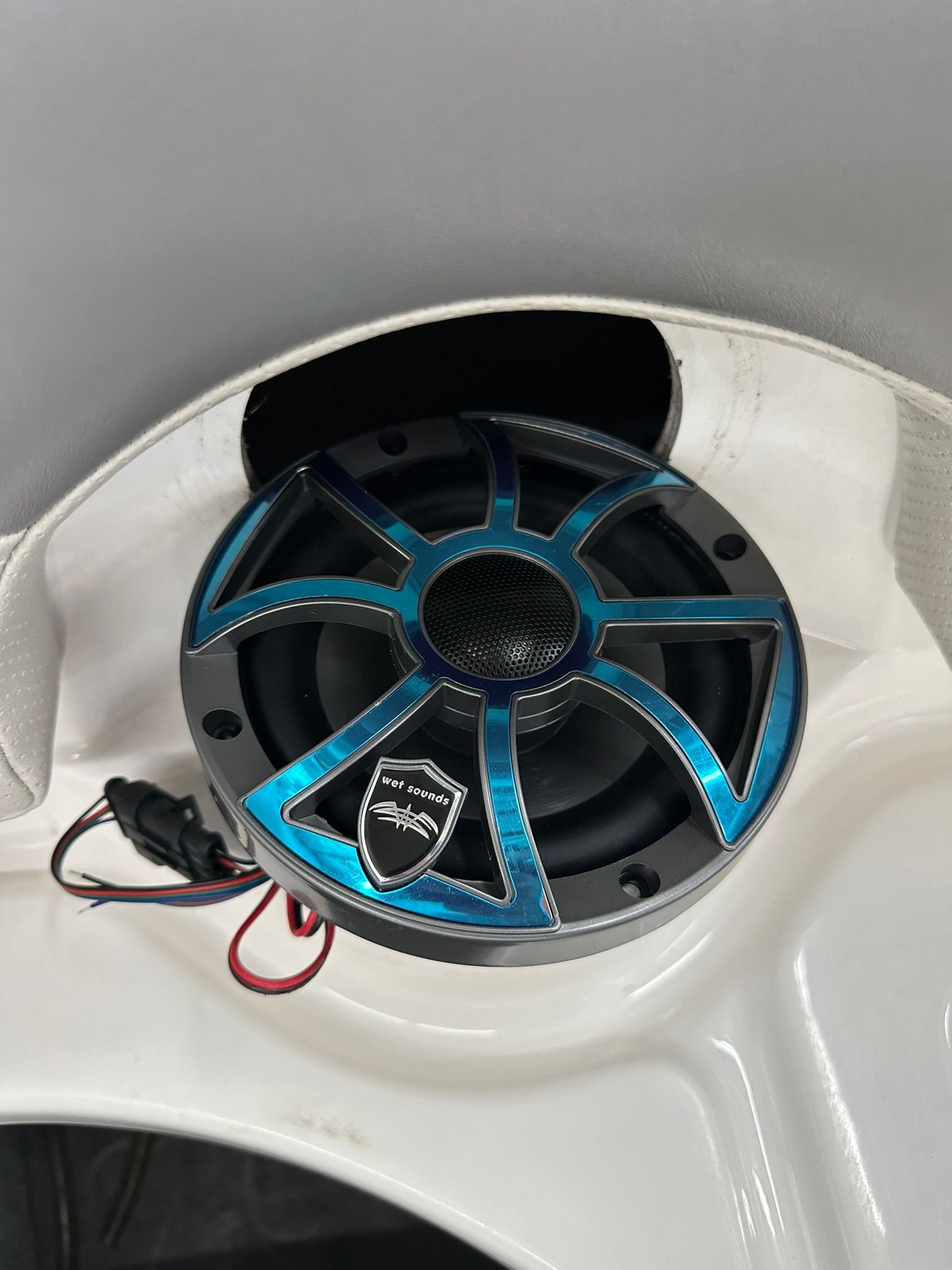 Marine speaker mounted in white boat panel, black and teal design, wires visible.