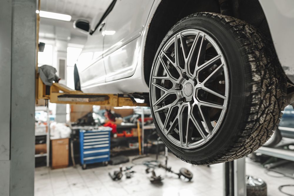 Car on hoist in workshop with tyre inspection and mechanical checks before long drive preparation