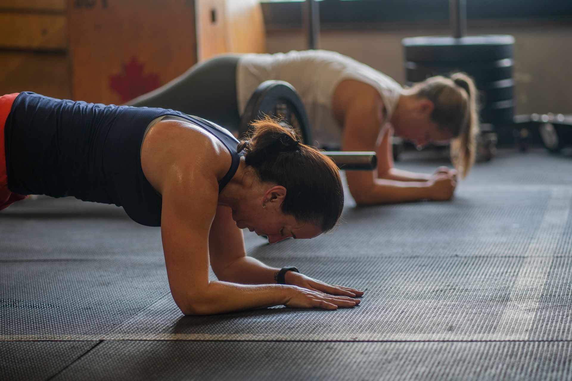 Two women are doing plank exercises on the floor in a gym.