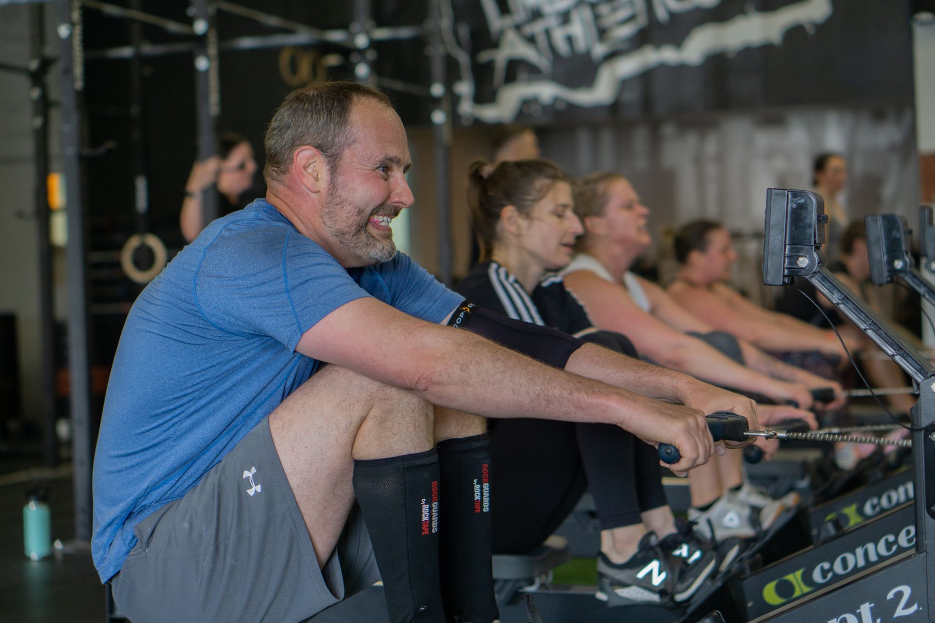 A group of people are riding rowing machines in a gym.