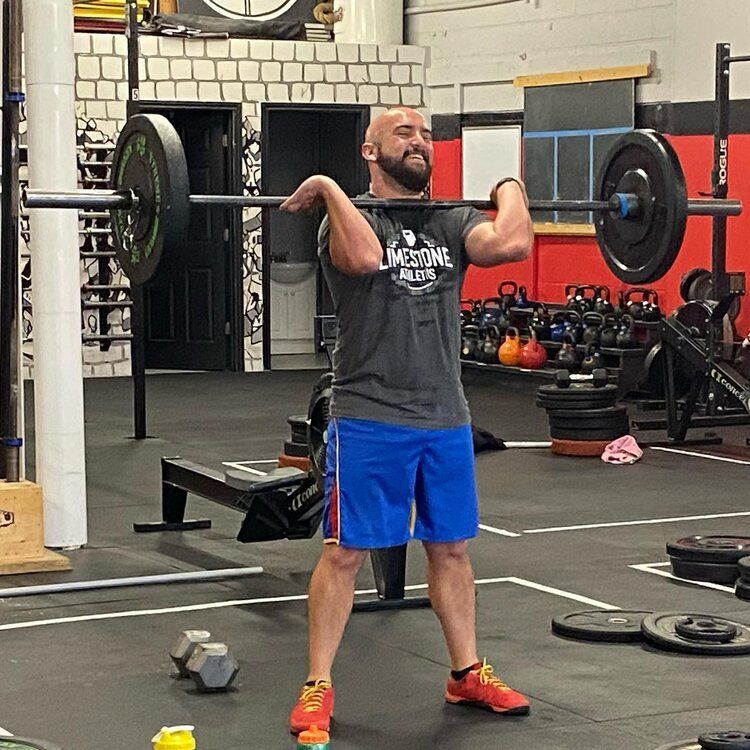 A man is lifting a barbell in a gym wearing a shirt that says onetime