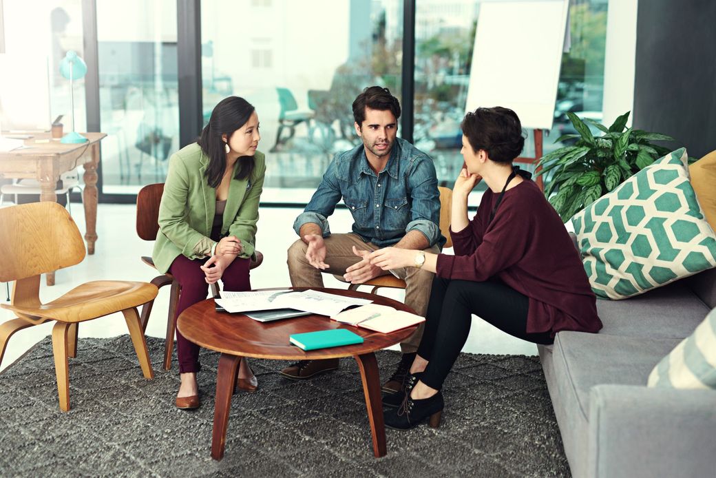 Three people discussing papers around a coffee table in a modern living room.