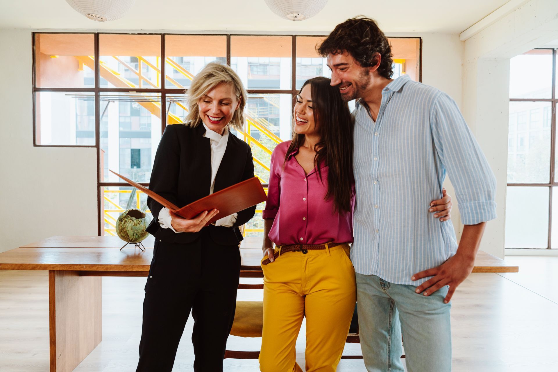 Three coworkers smiling over an open folder in a bright office room