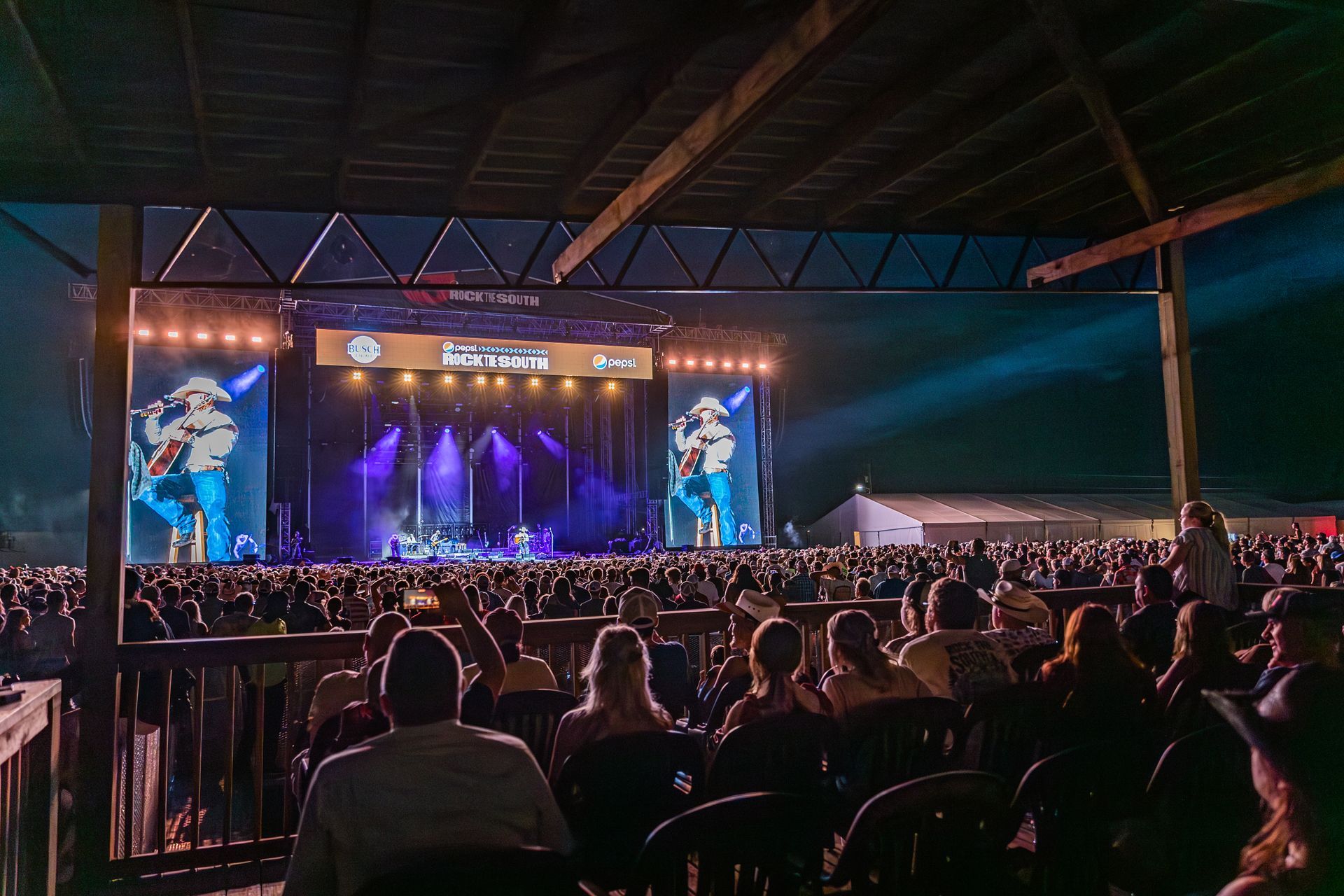 A crowd of people are sitting in front of a stage at a concert.