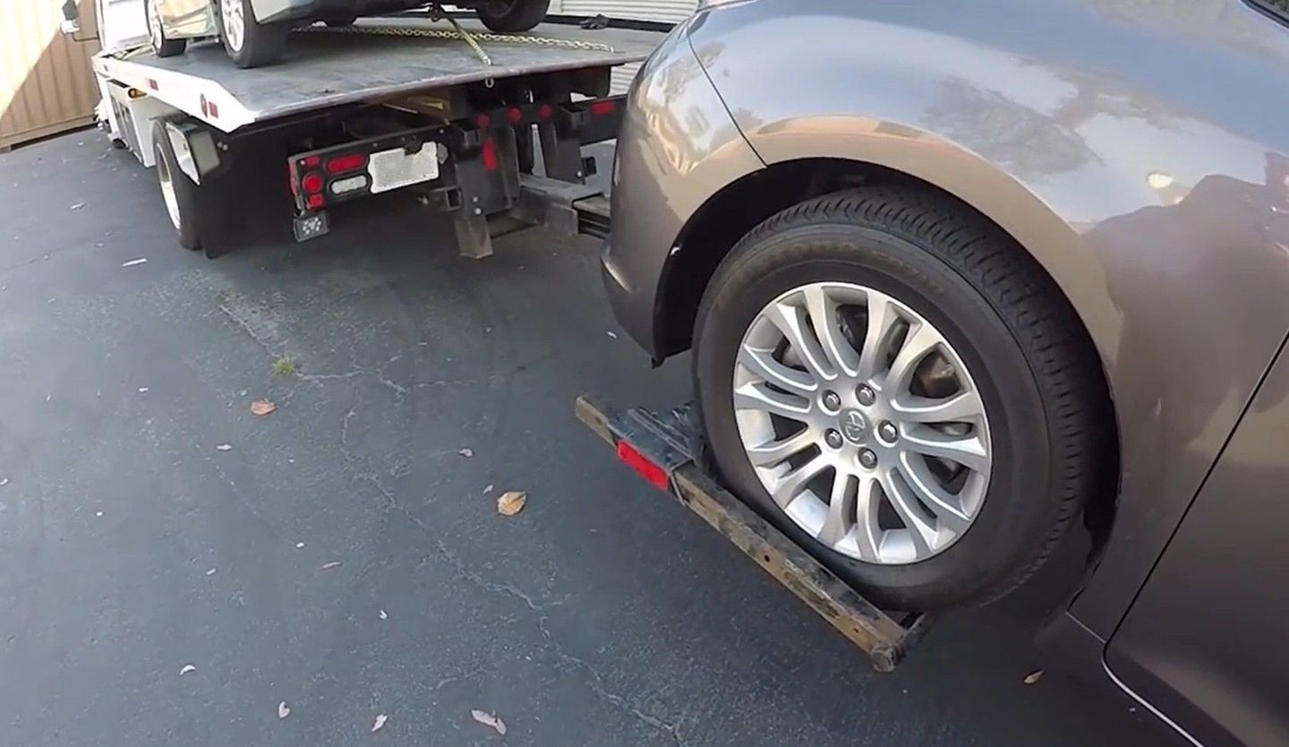 A car on a flatbed tow truck with another car on a dolly.