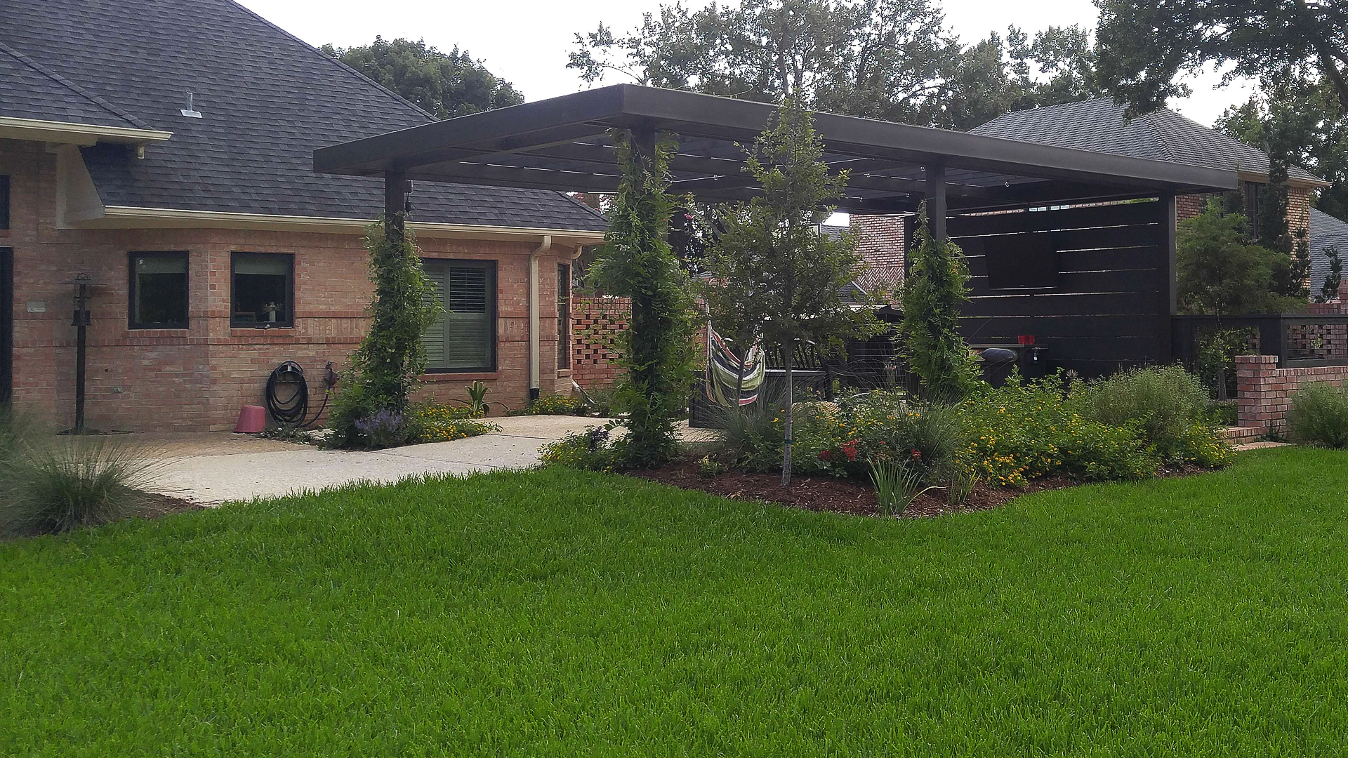A house with a pergola and a lush green lawn in front of it.