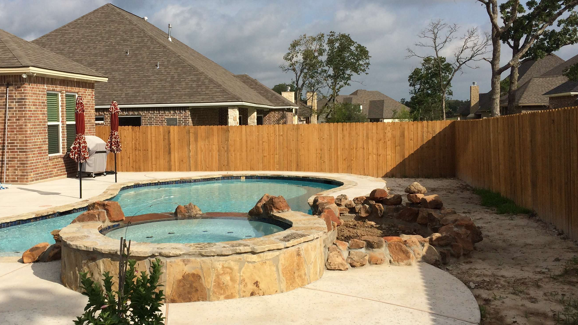 A wooden fence surrounds a large swimming pool in a backyard.