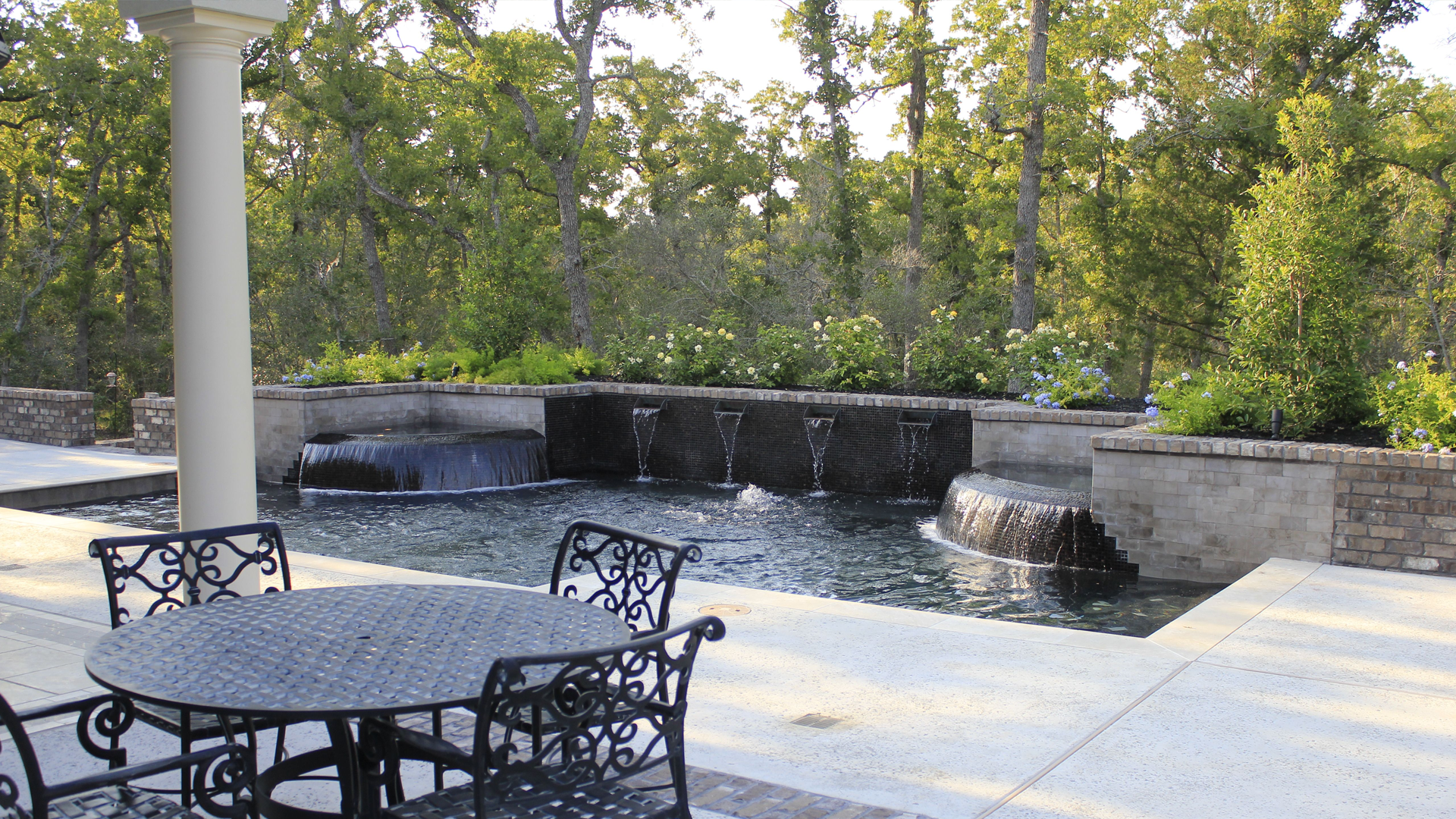 A patio with a table and chairs and a fountain in the background