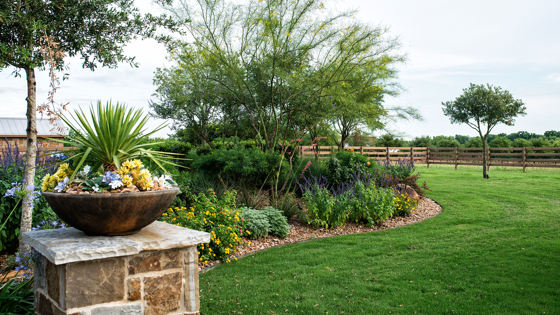 A garden with a stone pillar and a bowl of flowers in the middle of it.