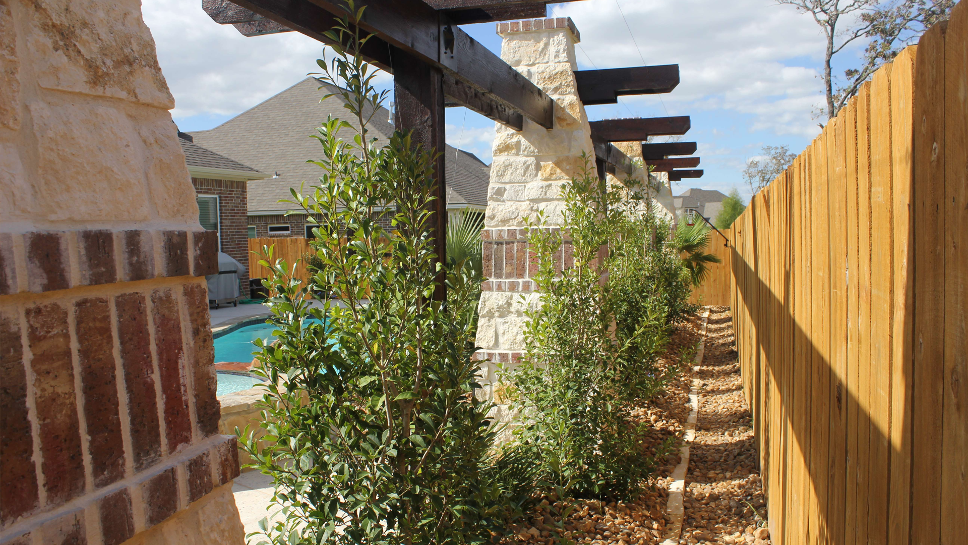 A wooden fence surrounds a brick wall and a swimming pool.