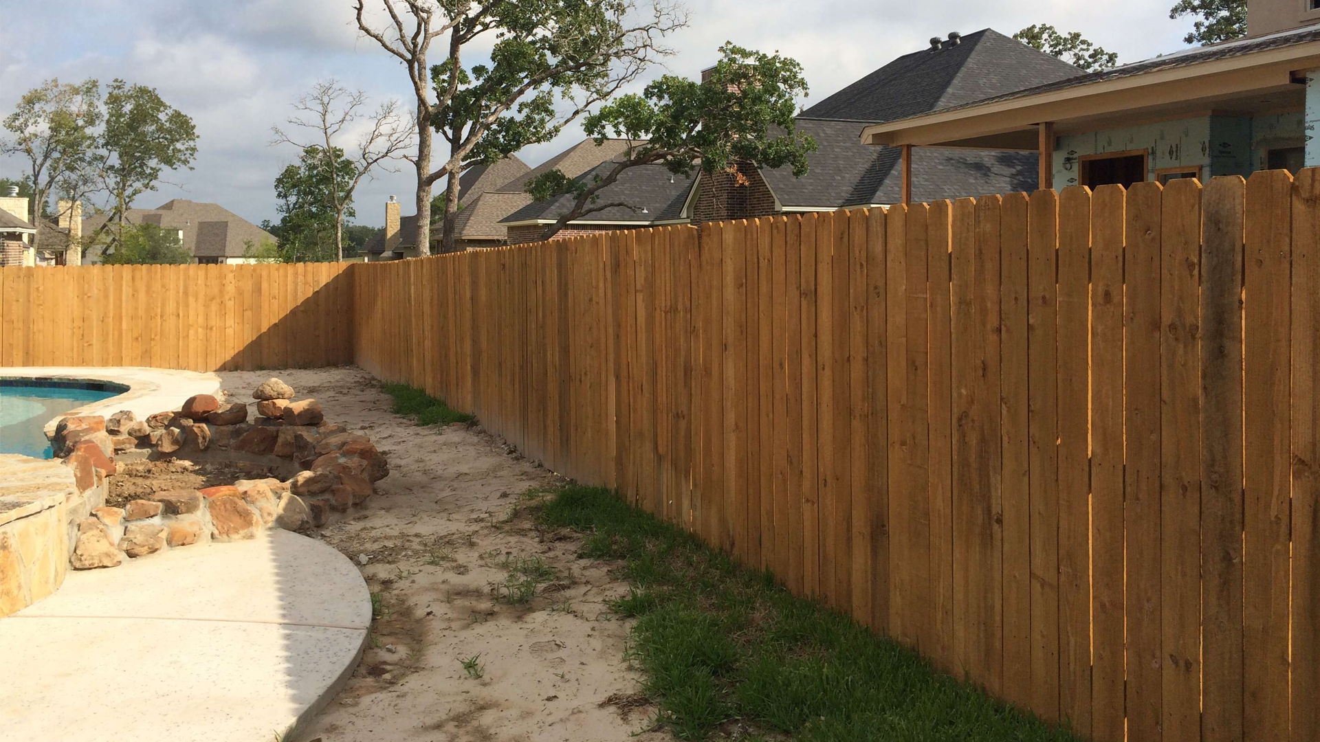 A wooden fence surrounds a swimming pool in a backyard.