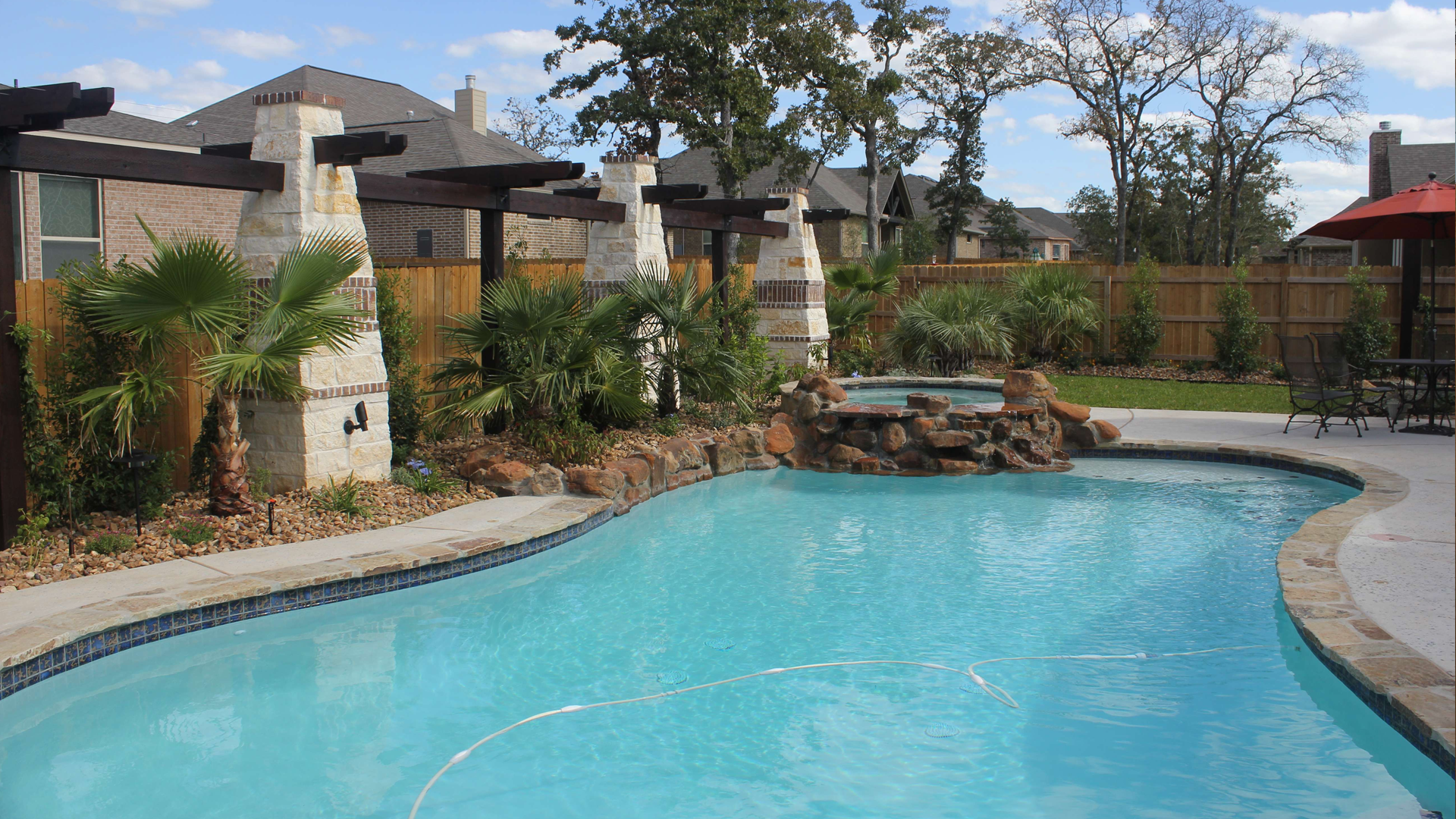 A large swimming pool with a waterfall in the backyard of a house.