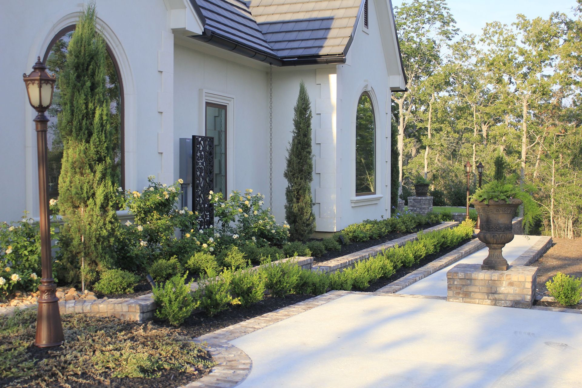 A white house with a black roof is surrounded by trees and bushes.
