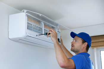 A man is fixing an air conditioner with a screwdriver.
