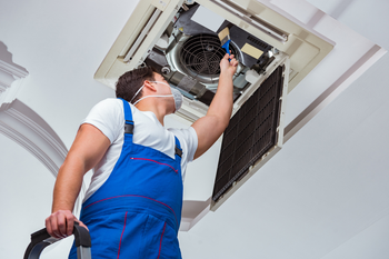 A man is cleaning a ceiling fan with a vacuum cleaner.
