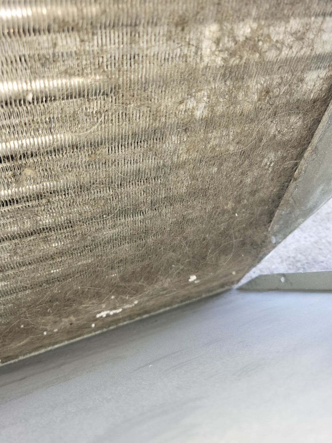 A close up of a dirty air conditioner coil on a white surface.