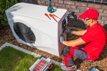 A man in a red shirt is working on a heat pump.
