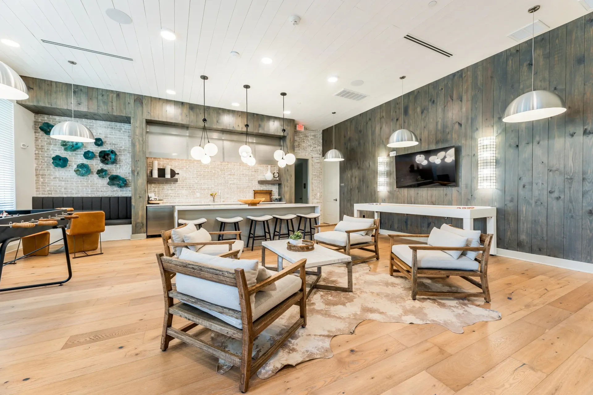 Spacious lounge area with foosball table, shuffleboard, bar seating, and comfortable chairs.
