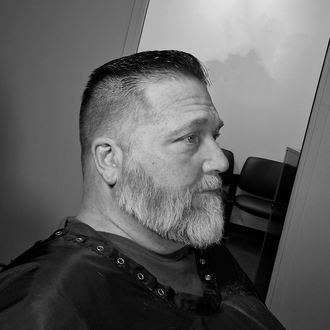 Black-and-white profile portrait of a bearded man seated indoors, looking to the right.