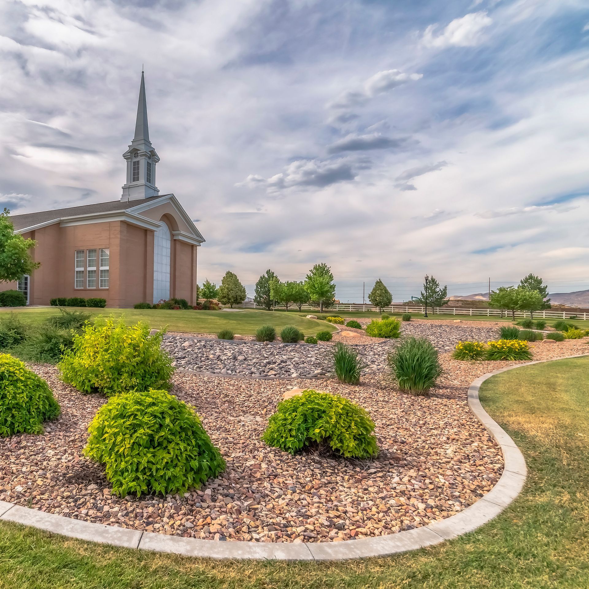 A church with a steeple is surrounded by gravel and bushes
