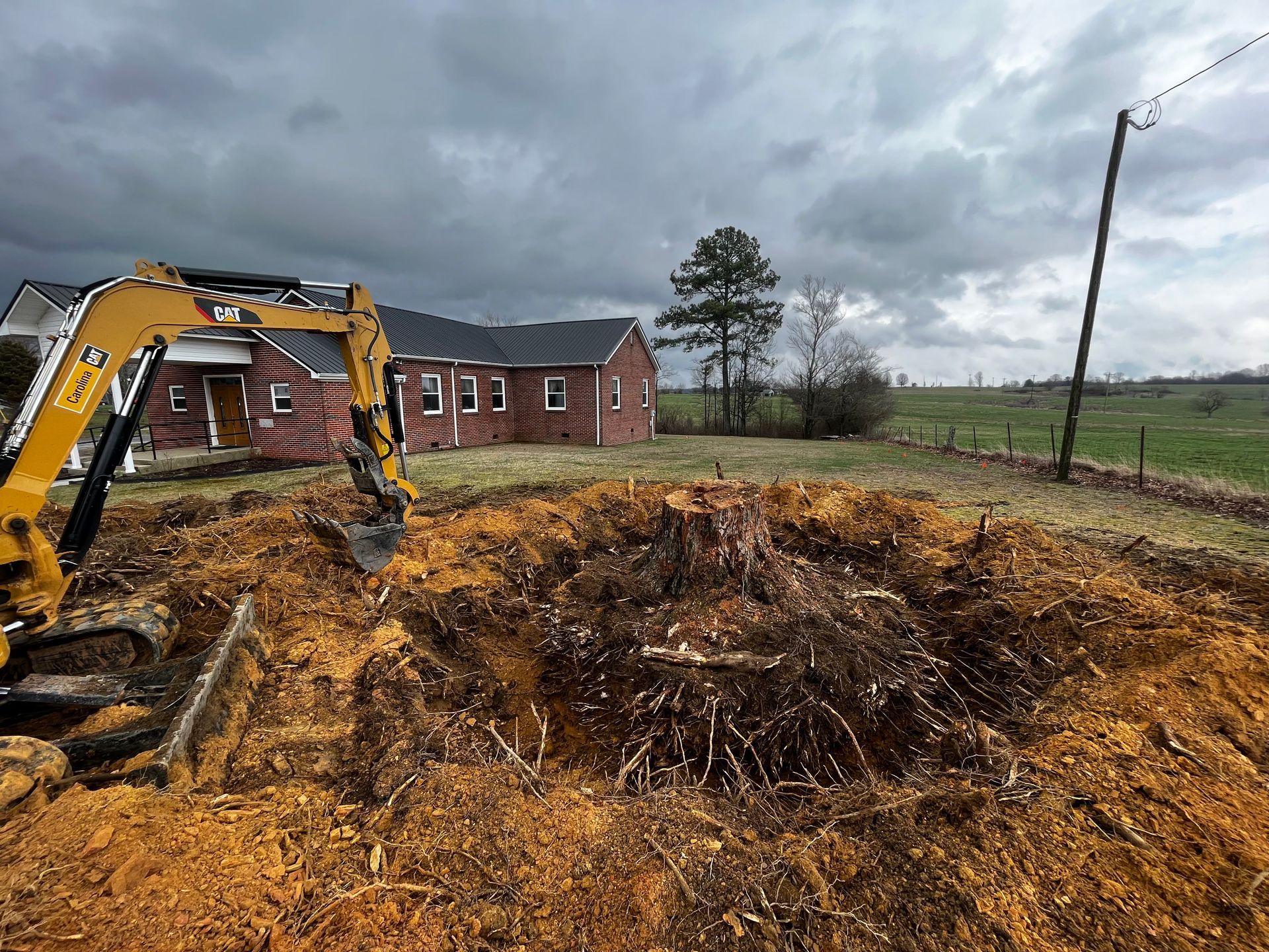 An excavator is digging a hole in the dirt in front of a house.