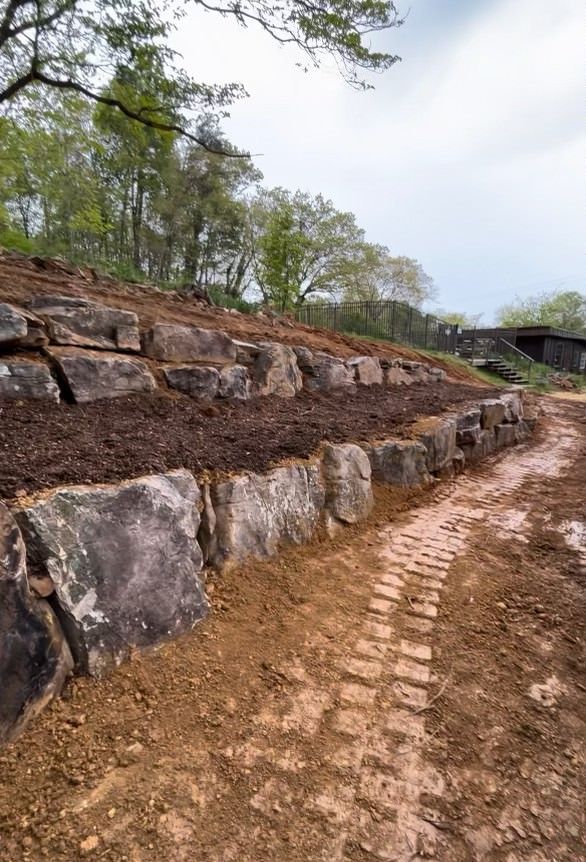 A dirt road going through a rocky hillside with trees in the background.
