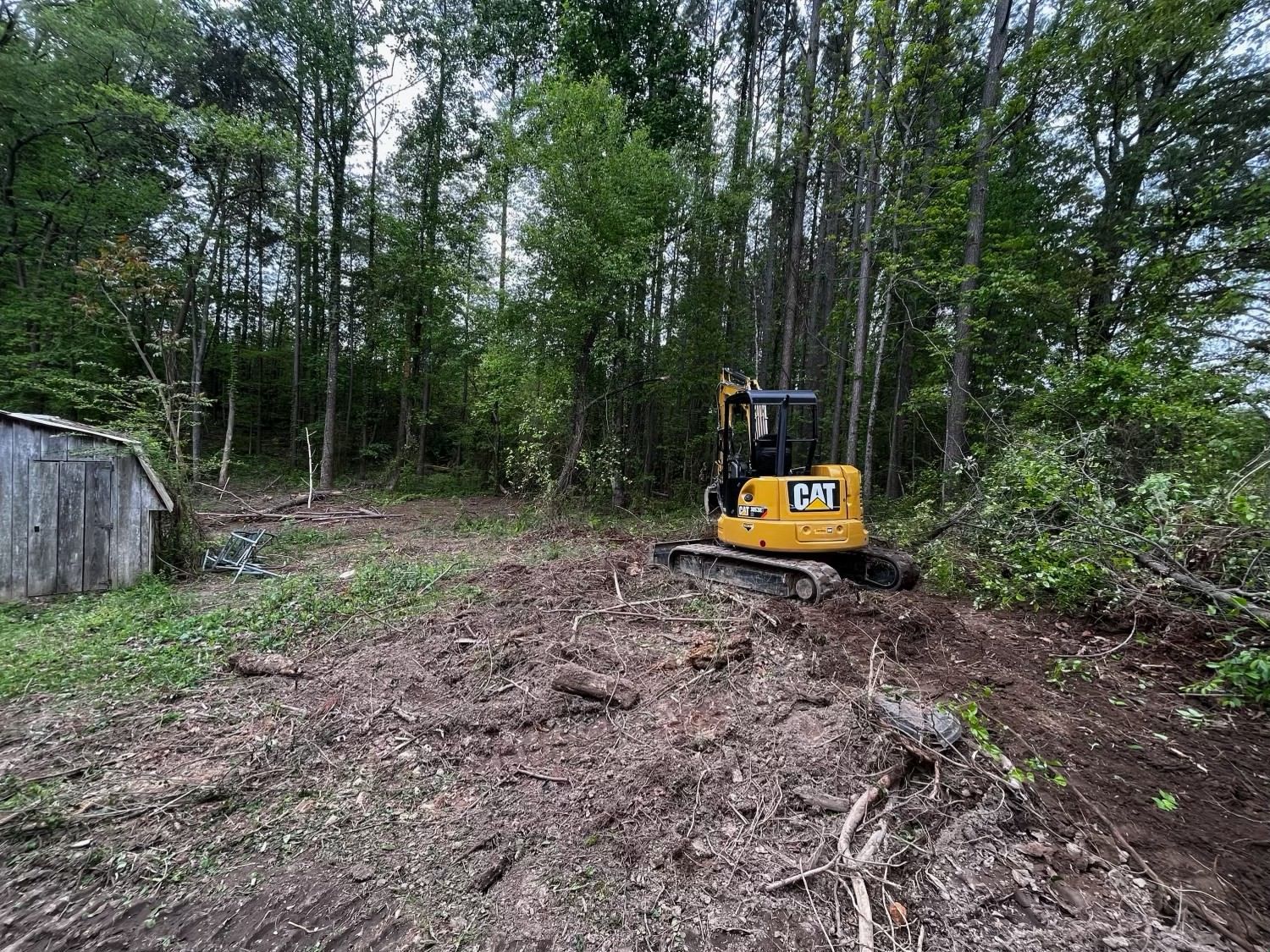 A yellow excavator is working on a dirt road in the woods.