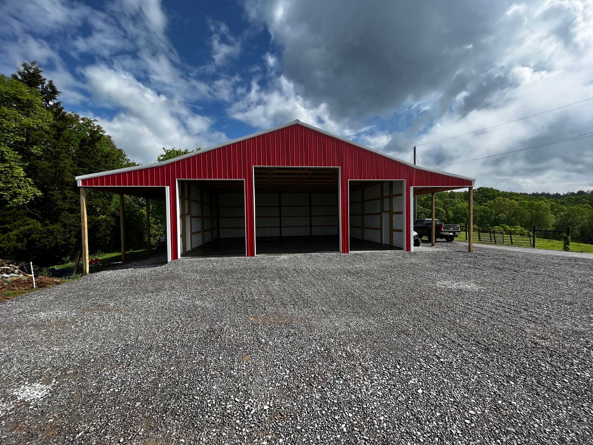 A red barn is sitting on top of a gravel driveway.