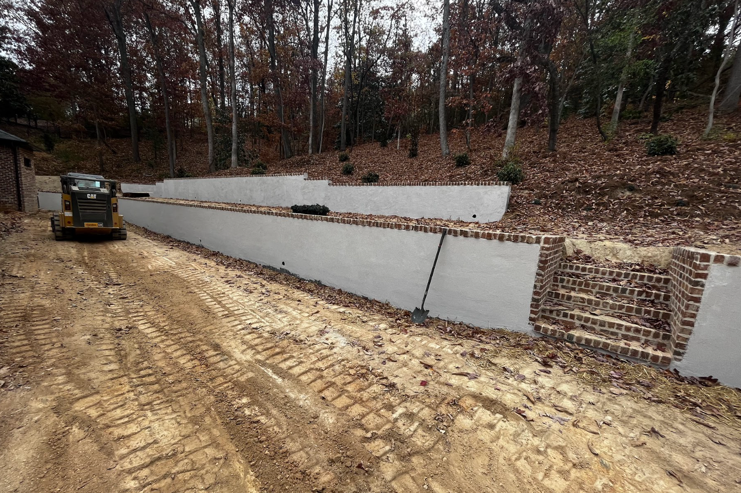 A bulldozer is driving down a dirt road next to a brick wall.