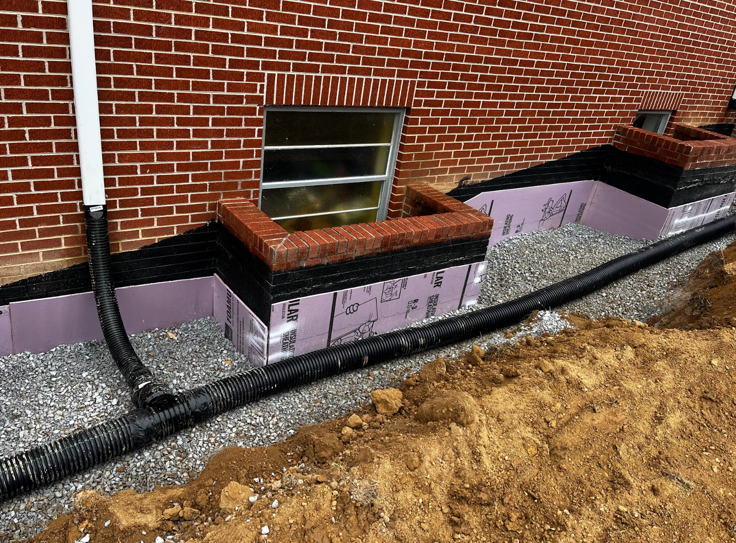 A brick wall with a window and a drain pipe