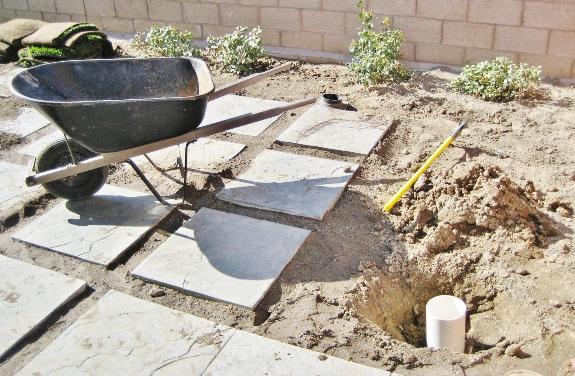 A wheelbarrow is sitting in the dirt next to a shovel.