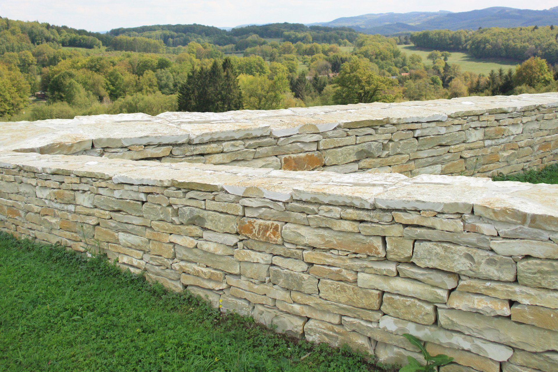 A stone wall with a view of a forest in the background