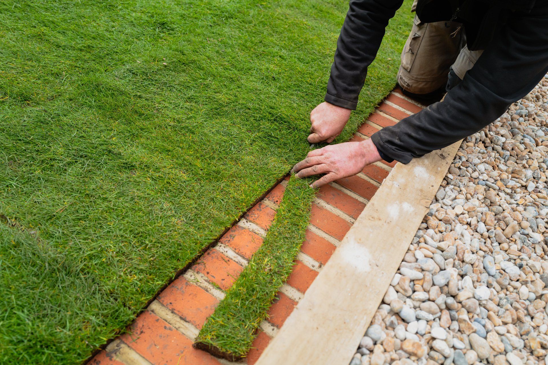A man is laying grass on a brick border.
