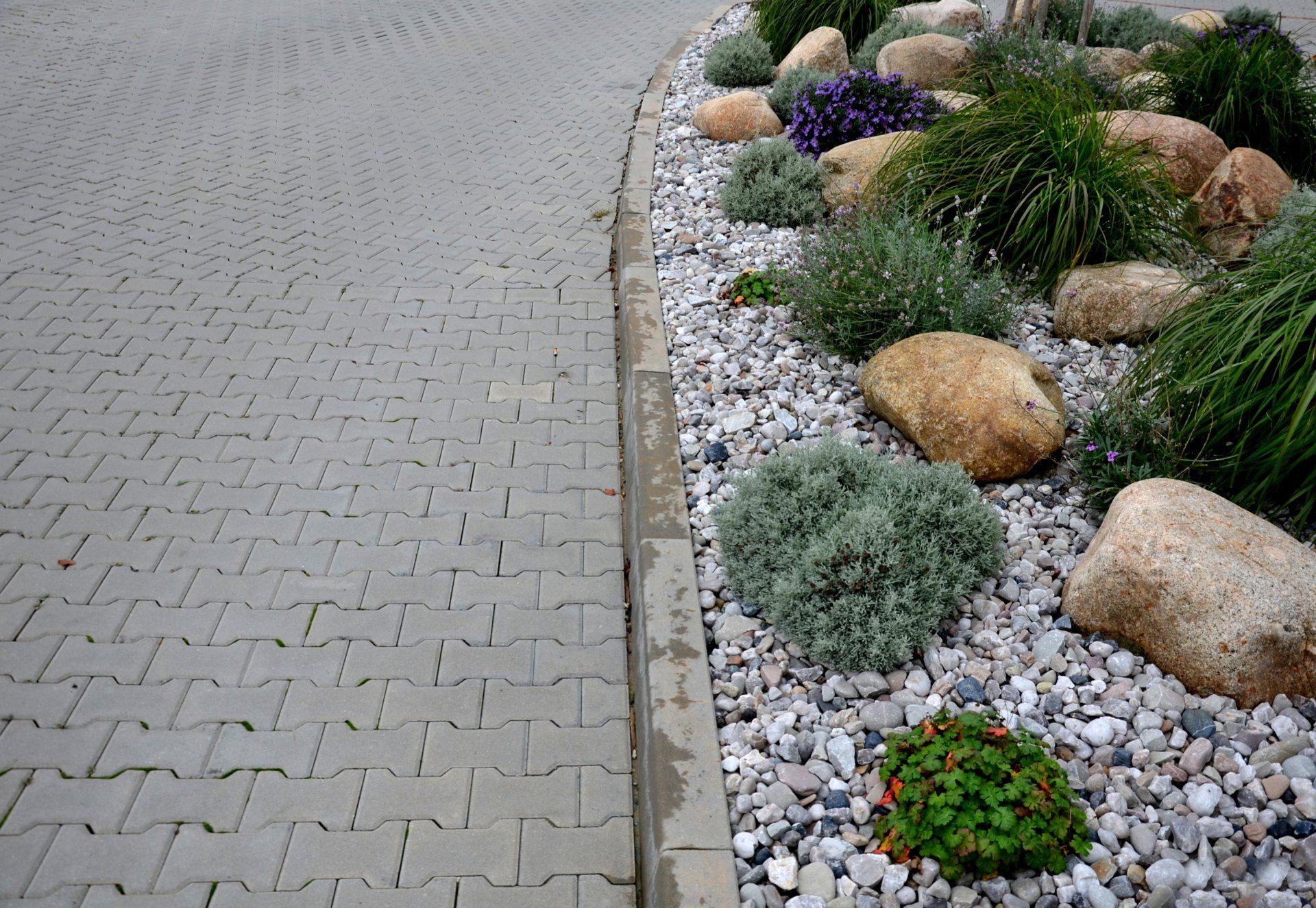 A brick walkway with rocks and plants on the side of it