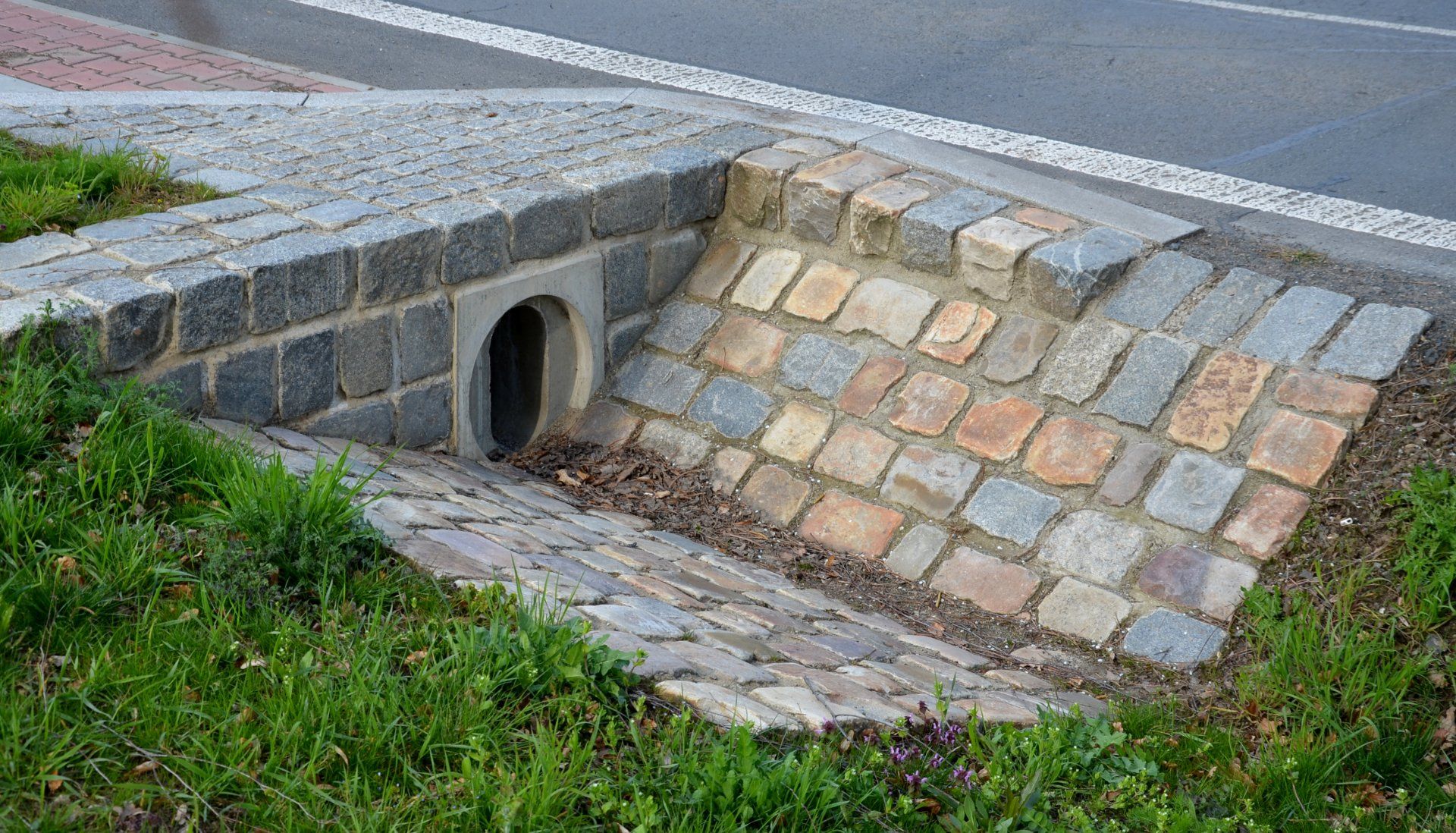 There is a drain in the grass next to the road.